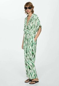 Groene en witte gestreepte jumpsuit met een wikkelontwerp, korte mouwen en zakken, gecombineerd met een paar zwarte zonnebrillen en slippers.