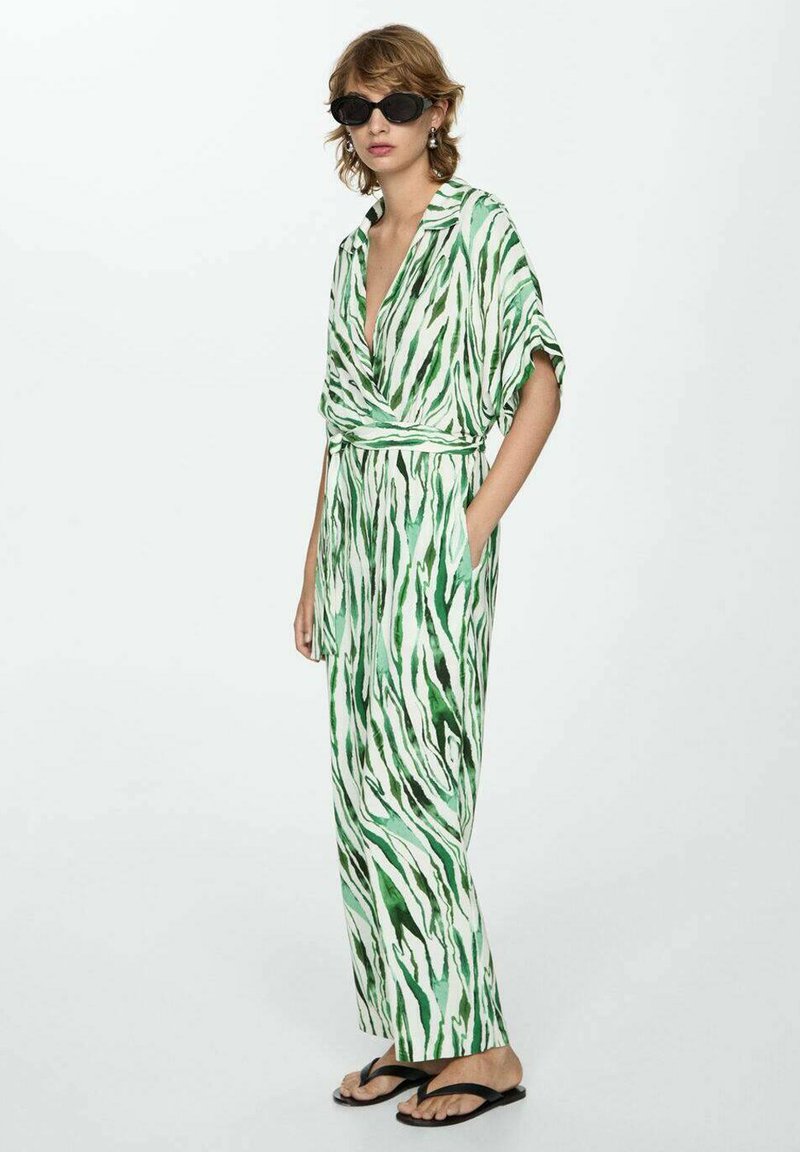 Groene en witte gestreepte jumpsuit met een wikkelontwerp, korte mouwen en zakken, gecombineerd met een paar zwarte zonnebrillen en slippers.