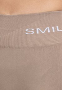 Beige leggings met een geribbeld patroon en een elastische tailleband, voorzien van de tekst "SMILE" in het wit aan de voorkant.