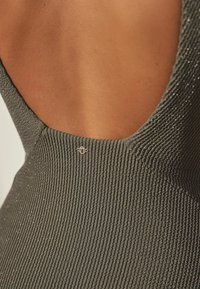 Ribbed olive green dress featuring a deep back neckline and a small metallic logo accent near the seam, highlighting the textured fabric.