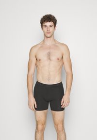 Zwarte boxershorts gemaakt van zachte stof met een elastische tailleband waarop het Calvin Klein-logo staat. Glad textuur, aansluitend ontwerp.