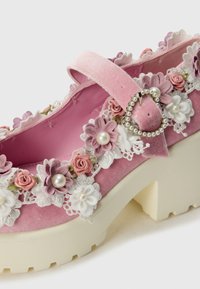 Roze fluwelen Mary Jane-schoen met bloemversieringen, kantafwerking en een gesp met een parelaccent. Dikke witte plateauzool.