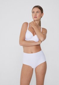 Bílá bezešvá podprsenka a set s vysokým pasem. Hladká tkanina, zakřivený tvar košíčků, nastavitelné ramínka, minimalistický styl bez viditelných švů.