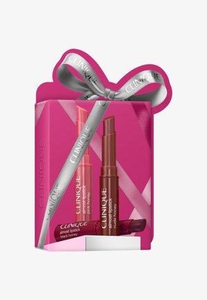 Caja de regalo rosa atada con cinta plateada de Clinique, que contiene tres tonos de Clinique Almost Lipstick: rosa, nude y baya oscura.