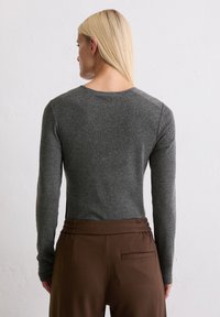 Szary longsleeve z miękkiego materiału, zestawiony z brązowymi spodniami w wysokim stanem, które mają tylną kieszeń i marszczone detale.