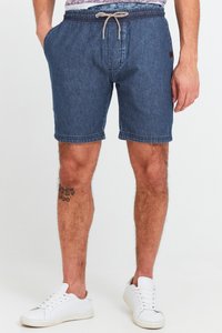 Shorts din denim de culoare albastru închis, cu talie elastică și șnur, dotate cu buzunare laterale și tivuri cusute, asortate cu adidași albi.