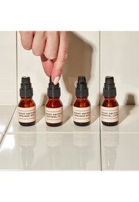 Vier bernsteinfarbene Flaschen mit schwarzen Pumpen, beschriftet mit "Night Switch" und unterschiedlichen Inhalten, auf einer weißen Fliesenoberfläche platziert.