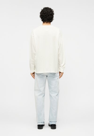 Μακρυμάνικο, εκρού πουκάμισο με άνετη εφαρμογή, συνδυασμένο με ανοιχτόχρωμα μπλε τζιν. Το πουκάμισο διαθέτει απλή, λεία υφή.