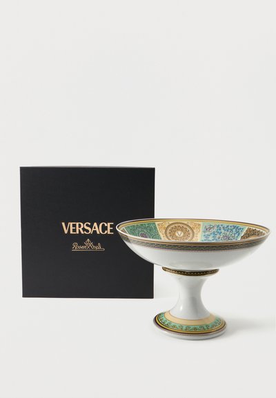 Λευκό πορσελάνινο μπολ σε βάση με περίτεχνα μοτίβα σε χρυσό και τιρκουάζ δίπλα σε μαύρο κουτί με την ετικέτα Versace Rosenthal.