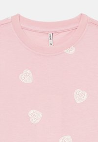 Lys rosa t-skjorte med hvite hjerteformede trykk og teksten "Girl Power". Myk stoff, rund hals og korte ermer.
