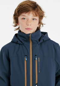Giacca a vento navy con cappuccio regolabile, zip marroni e dettagli blu. Presenta tasche frontali e un logo sul lato. Tessuto liscio.