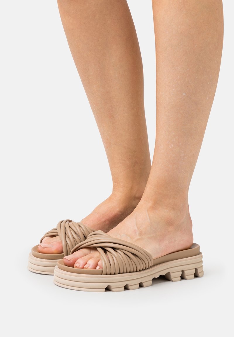 Sandales à glissière beige nouées avec une semelle épaisse et texturée, présentant des détails en relief, mettant en valeur un matériau doux et flexible pour le confort.