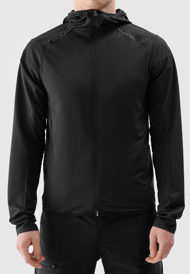 Zwarte lichte ritsjack met een capuchon. Heeft een gestructureerd oppervlak en een getailleerd ontwerp, met lange mouwen en subtiele stikdetails.