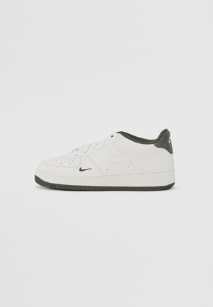Hvid lavtop-sneaker med sort sål, sort inderforing, lille sort swoosh nær tåen, større prægede swoosh på siden og snørebånd foran.