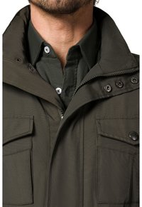 Oliwkowa kurtka z zamkiem błyskawicznym z przodu, stójką i dwiema kieszeniami na piersi. Posiada metalowe zatrzaski i wytrzymałą teksturę materiału.