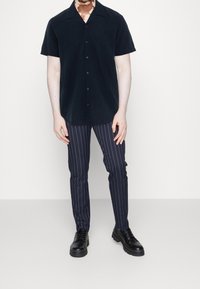 Černá košile s krátkým rukávem na knoflíky; tmavě modré pruhované slim-fit kalhoty; černé boty; hladká látka; uvolněný střih s klasickým límcem.