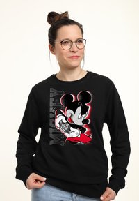 Sudadera negra con un gráfico de Mickey Mouse sosteniendo un controlador de juego, con el texto en negrita "MICKEY" al lado en escala de grises.