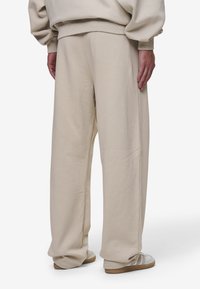 Beige sweatpants with a relaxed fit, cotton blend material, side seams, and hidden pockets, featuring wide legs and elastic waist.