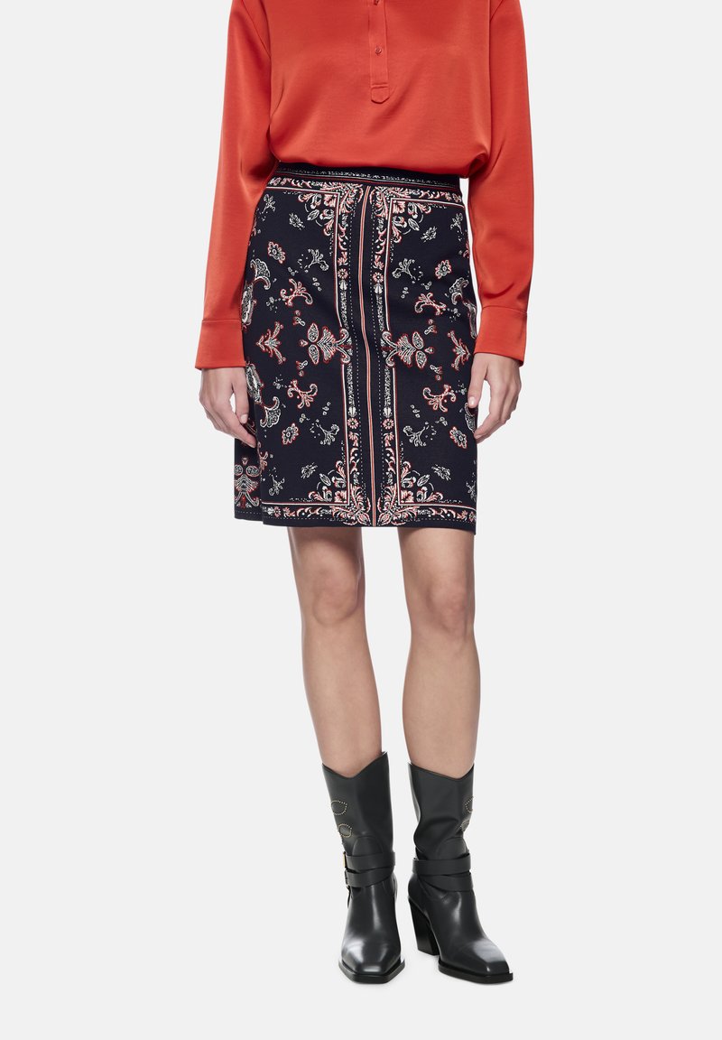 Floral-patterned skirt in dark navy with red and white accents, featuring a cinched waist and side pockets. Paired with black heeled boots.
