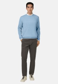 Lichtblauwe trui van zachte brei, ronde halslijn, gedragen over een wit shirt. Grijze textuurbroek en crèmekleurige sneakers met zwarte veters.