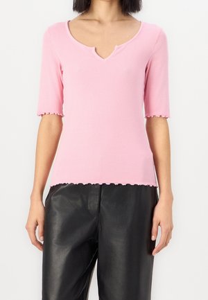 Różowy prążkowany sweter z dzianiny z dekoltem w serek, krótkimi rękawami i falistymi krawędziami, zestawiony z czarnymi skórzanymi spodniami.