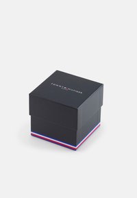 Boîte cadeau en carton noir avec un couvercle, arborant le logo "TOMMY HILFIGER" sur le dessus et un accent rayé rouge, blanc et bleu à la base.