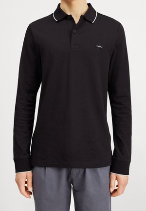 Polo a maniche lunghe nera realizzata in cotone, con colletto bianco rifinito e logo sul petto, taglio dritto e maniche aderenti.