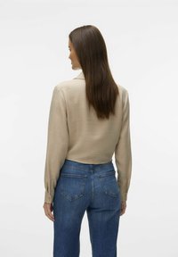 Blusa beige a maniche lunghe con finitura testurizzata, abbinata a jeans blu a vita alta con design classico a cinque tasche e cuciture in evidenza.