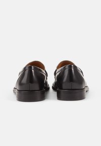 Black leather shoes with a smooth finish, round toe, low stacked heel, and buckle detail on the side. Designed for formal wear.