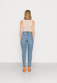 Top beige sin mangas con estampado de cebra, combinado con unos vaqueros de tiro alto en azul claro y zapatos de tacón cuadrado en color naranja. Vista posterior.