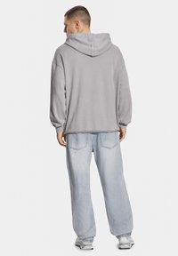 Szary hoodie w luźnym kroju z prążkowanymi mankietami, w połączeniu z jasnoniebieskimi szerokimi dżinsami i białymi trampkami. Prosty design z luźnym fasonem.