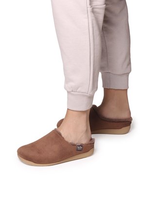 Bruine instapslippers met een zachte, textuur bovenkant en een fuzzy manchet. Dunne zool, eenvoudig ontwerp en een klein label aan de zijkant.
