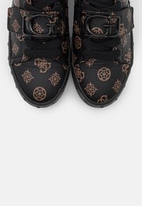 Černé tenisky s texturovaným koženým svrškem s hnědým geometrickým vzorem loga, nastavitelné popruhy a kulaté ozdobné kování.