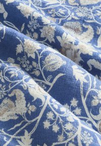 Tână de culoare albastră cu un design floral în alb, având modele complexe și o țesătură texturată. Apariție moale, ușor șifonată.