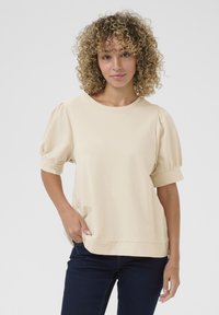 Top beige con maniche a palloncino e scollatura rotonda, realizzato in un tessuto morbido. Presenta una vestibilità comoda e dettagli di cucitura sottili all'orlo.