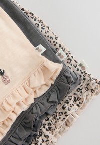 Pile de trois vêtements pour bébé avec des bords volantés, en pêche, gris, et imprimé léopard, chacun avec une petite étiquette ananas.