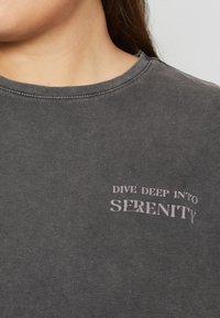 Camiseta de algodón gris oscuro con cuello redondo y mangas cortas que presenta el texto blanco "INMERSETE EN LA SERENIDAD" en el frente.
