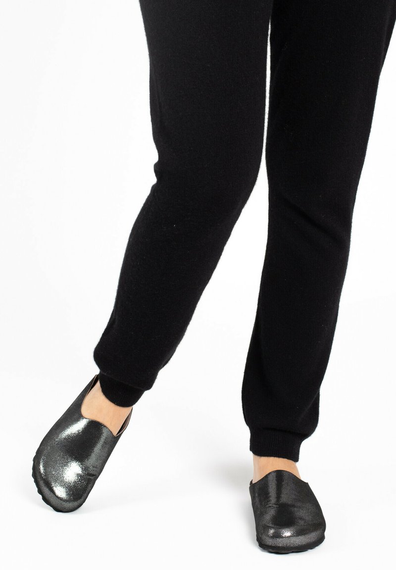 Joggers ajustados negros combinados con zapatos negros de slip-on brillantes, que presentan una textura suave y un diseño de punta redondeada, resaltando su estilo casual.