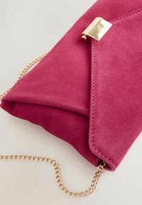 Rosa Wildleder-Clutch mit Umschlagdesign, versehen mit einem goldenen Metallverschluss und einem abnehmbaren goldenen Kettenriemen. Glatte Textur mit tonaler Naht.