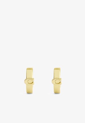 Pendientes de metal en tono dorado con un diseño minimalista, que presentan una forma plana y un sutil detalle de logotipo en el lateral. Textura suave y acabado pulido.