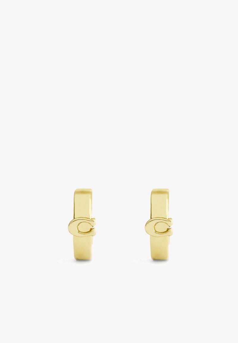 Pendientes de metal en tono dorado con un diseño minimalista, que presentan una forma plana y un sutil detalle de logotipo en el lateral. Textura suave y acabado pulido.