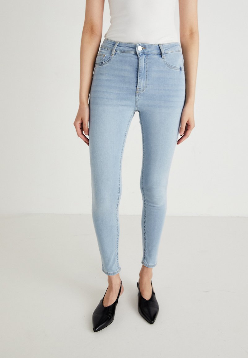 Ανοιχτό μπλε ψηλόμεσα skinny τζιν με λεία υφή, διαθέτουν πέντε τσέπες και τονική ραφή, συνδυασμένα με μαύρες μυτερές μπαλαρίνες.