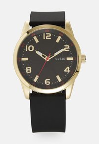 Black silicone strap watch with a gold case, black dial, and bold white hour markers. Red accents on the hands and bezel indicate seconds.