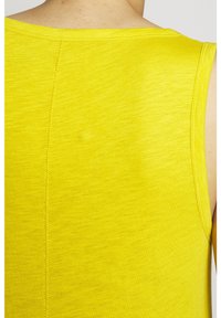 Keltainen hihaton toppi pehmeällä tekstuurilla, jossa on pyöreä kaula-aukko ja näkyvät saumat.