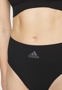Černé sportovní vysoké kalhotky s hladkou texturou a šedým logem Adidas na pase, s přiléhavým střihem.
