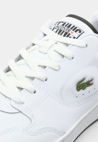 Sneaker alb din piele cu logo-ul brodat al crocodilului verde, sireturi albe plate, accent negru pe limbă și detalii cusute.