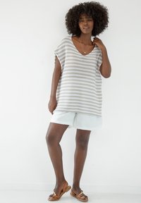 Pasiasty, lekki sweter w beżowo-białe paski, z dekoltem w kształcie litery V i krótkimi rękawami, w zestawieniu z jasnymi szortami i płaskimi sandałami.