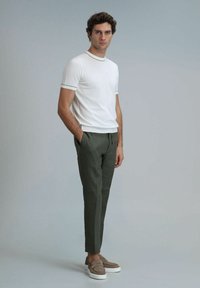 Weißes kurzärmliges T-Shirt mit schwarzem Saum, kombiniert mit taillierten olivgrünen Hosen und hellbraunen Slippern mit weißen Sohlen.