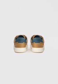 Pruunid tennisetooted tekstureeritud nahast ja siniste kangast aktsentidega, valge tallaga ja kontrastse punase brändinguga kanna peal.