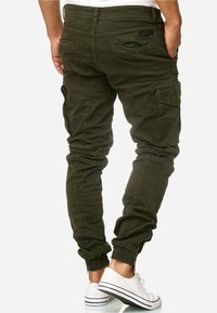 Pantaloni cargo verde oliva con caviglie elastiche, numerose tasche e una finitura morbida e testurizzata, caratterizzati da dettagli con tasche con cerniera.